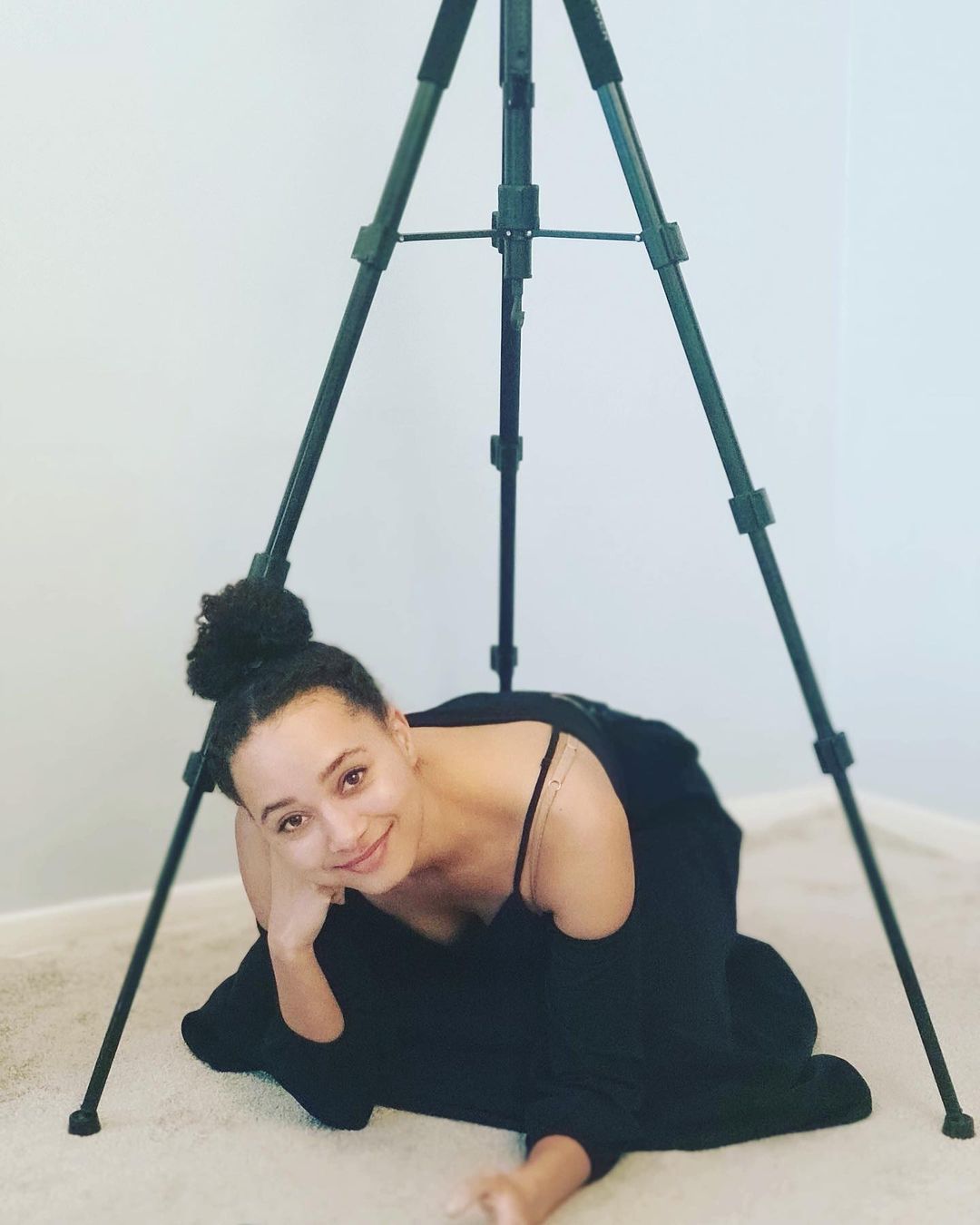 Emma Naomi in black dress sitting below a tripod stand