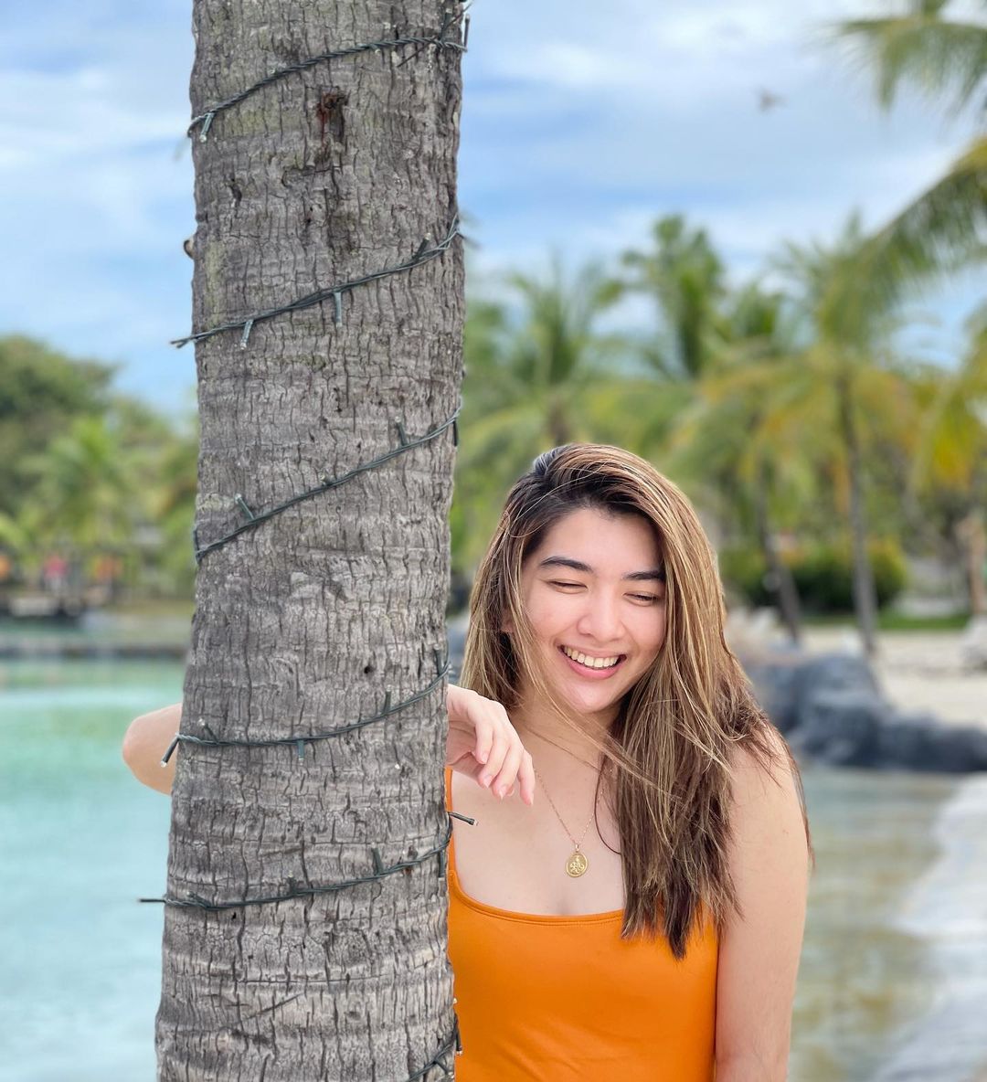 Pau Fajardo standing behind a tree in orange top