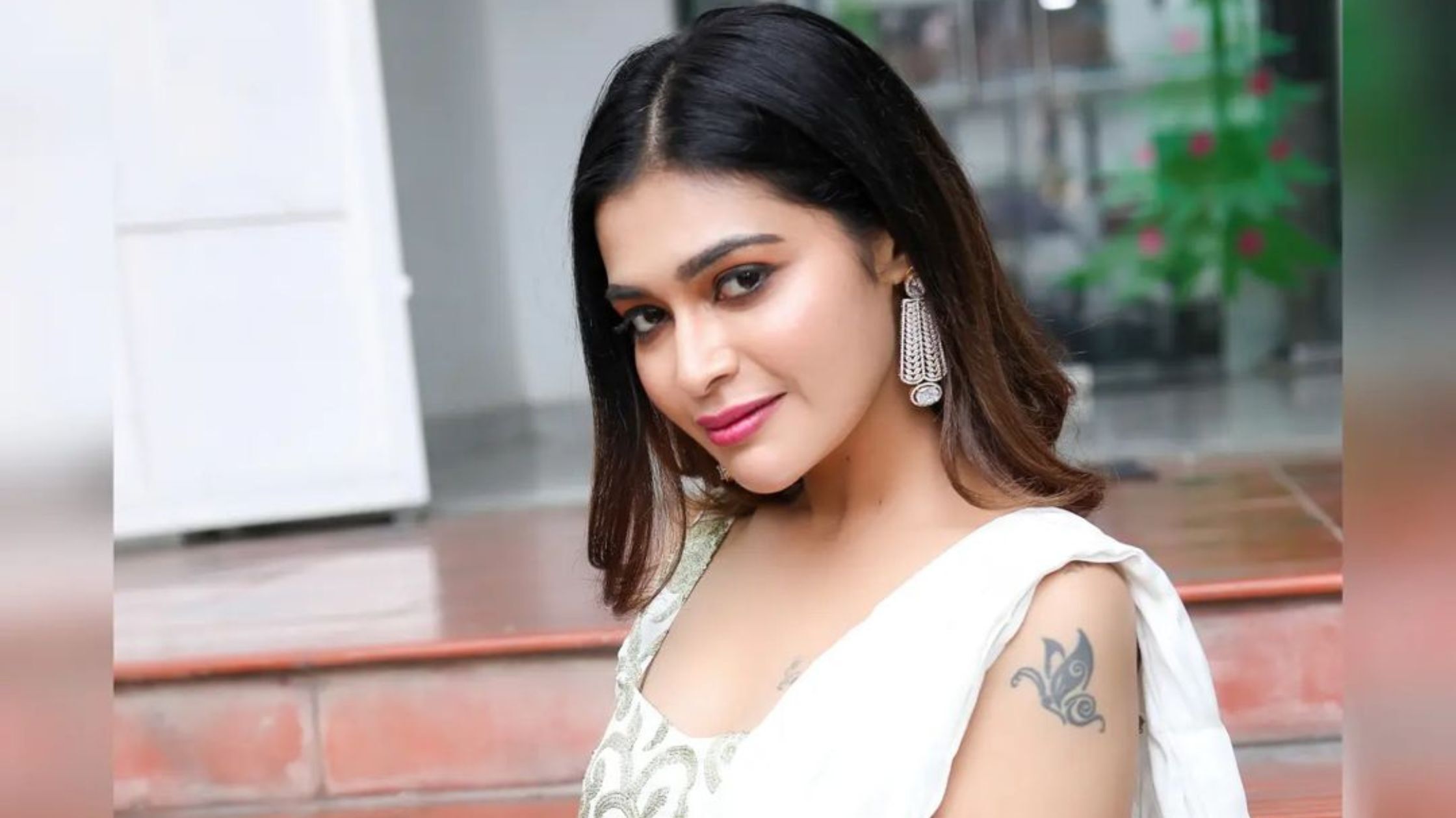 Dharsha posing in a white saree with a tattoo on her shoulder. 