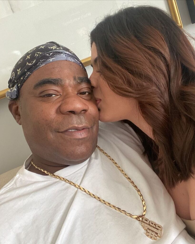 Tracy taking a selfie with his partner wearing gold chain.