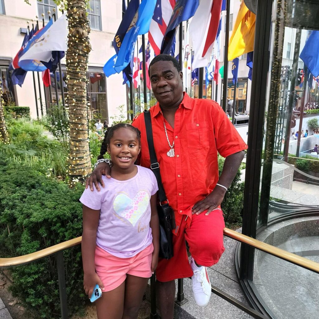 Tracy Morgan wearing red shirt and posing with his daughter in a street.