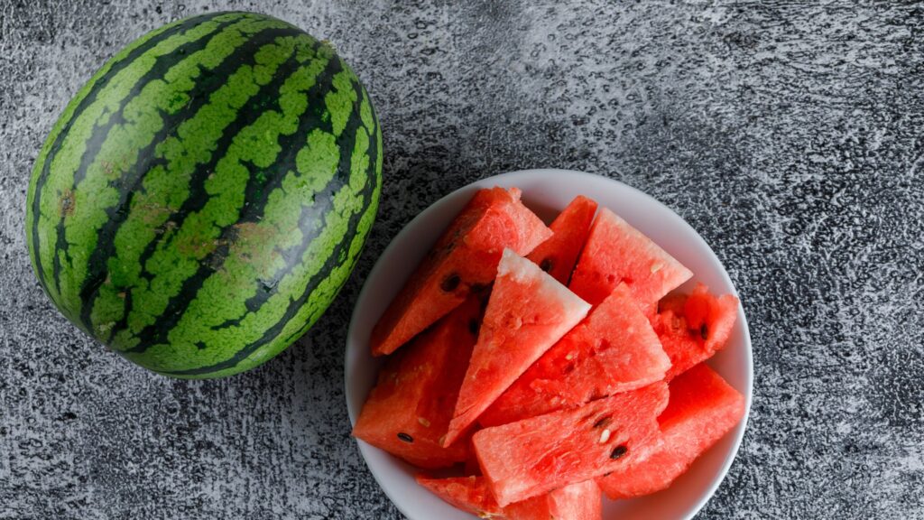 watermelon served in a white plate alongside a full watermelon on a table.