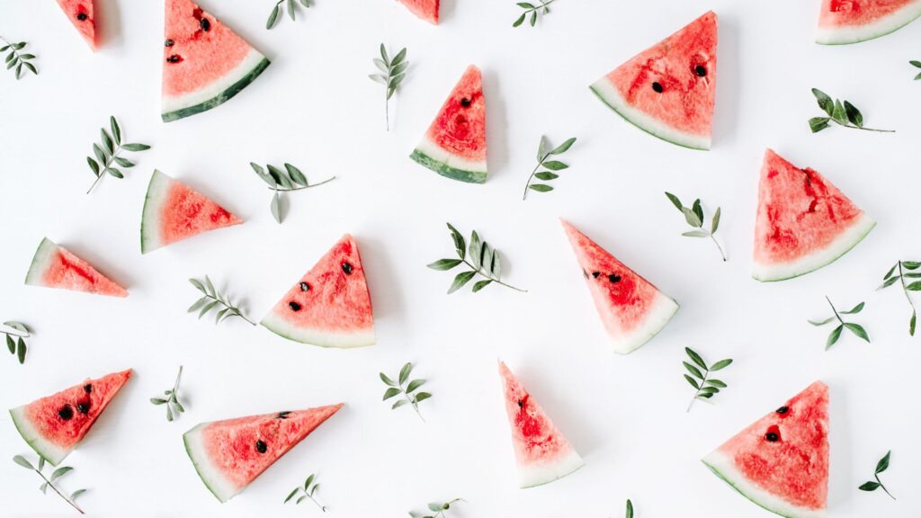 Multiple slices of watermelons placed on a white background along with leaves between them.