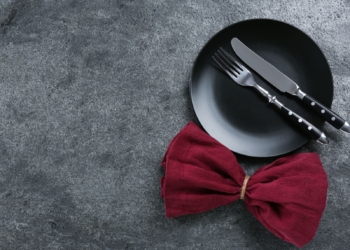 A black plate with fork and knife with a red bow on the table.