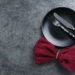 A black plate with fork and knife with a red bow on the table.