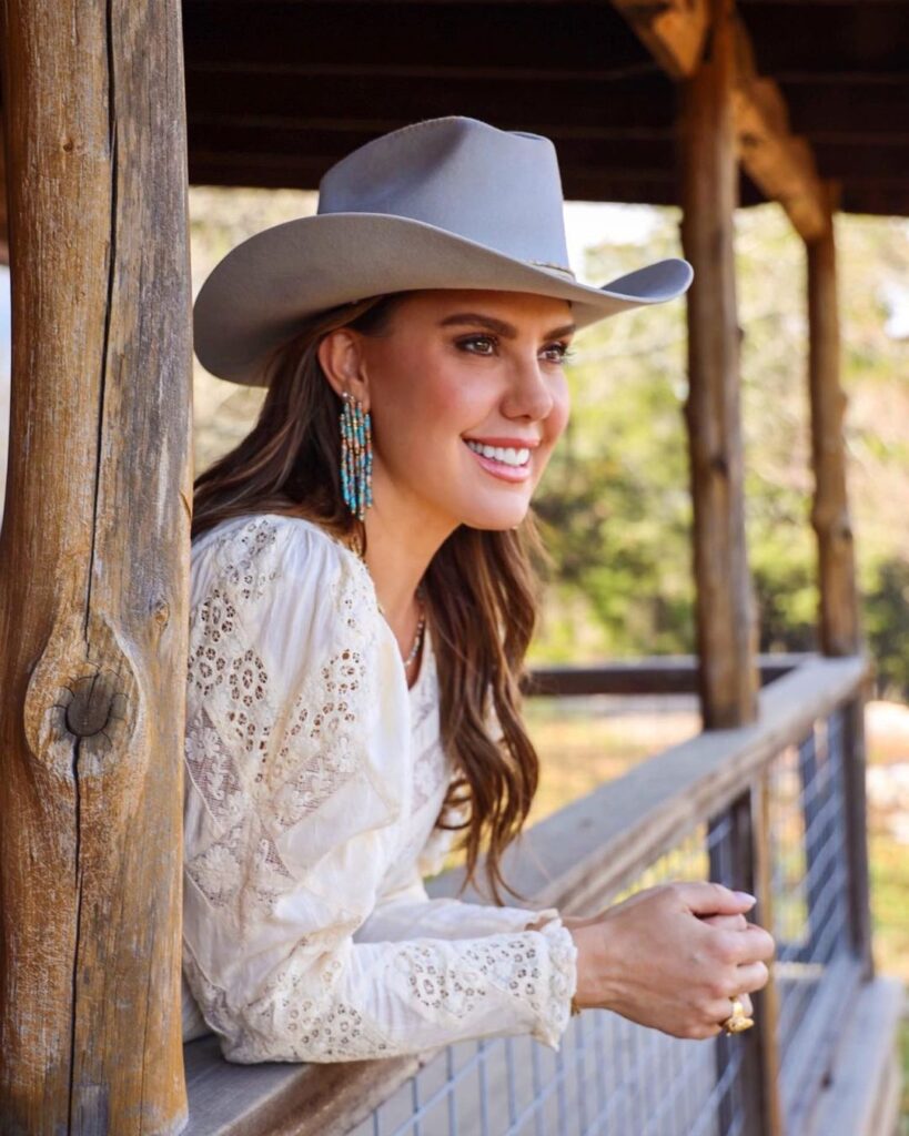 Kendra wearing a hat and white dress and looking towards the field.