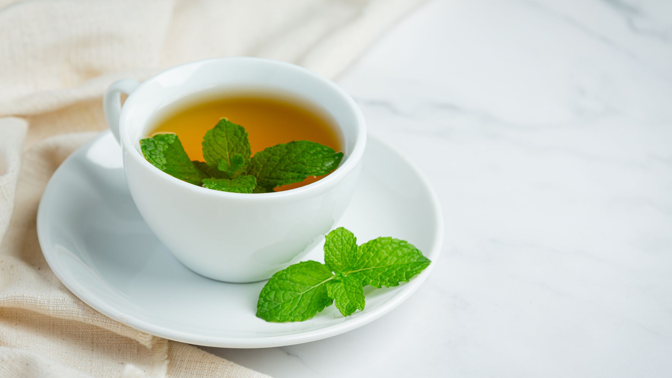 Mint tea served in a white cup and placed on a white table.
