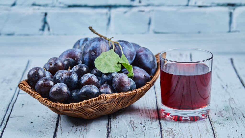 A prune juice glass and a basket of fresh prunes.