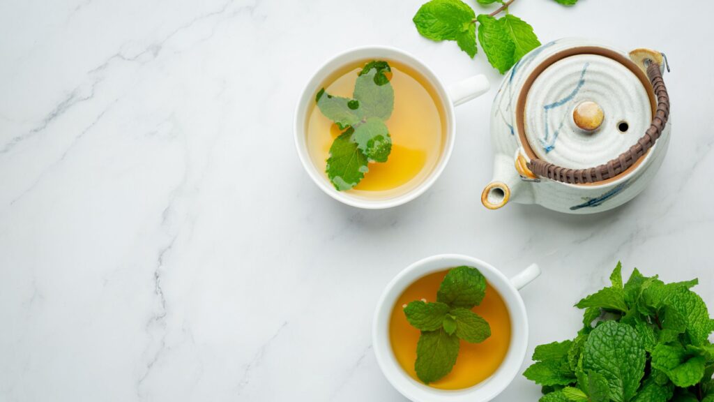 A tea pot and two cups full of spearmint tea is placed on a white table.