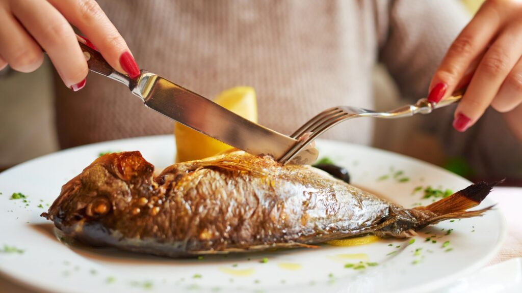 A female cutting in American style with knife and fork.