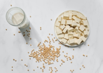 A plate full of raw tofu with soy milk in glass and some soy spread on the white table.
