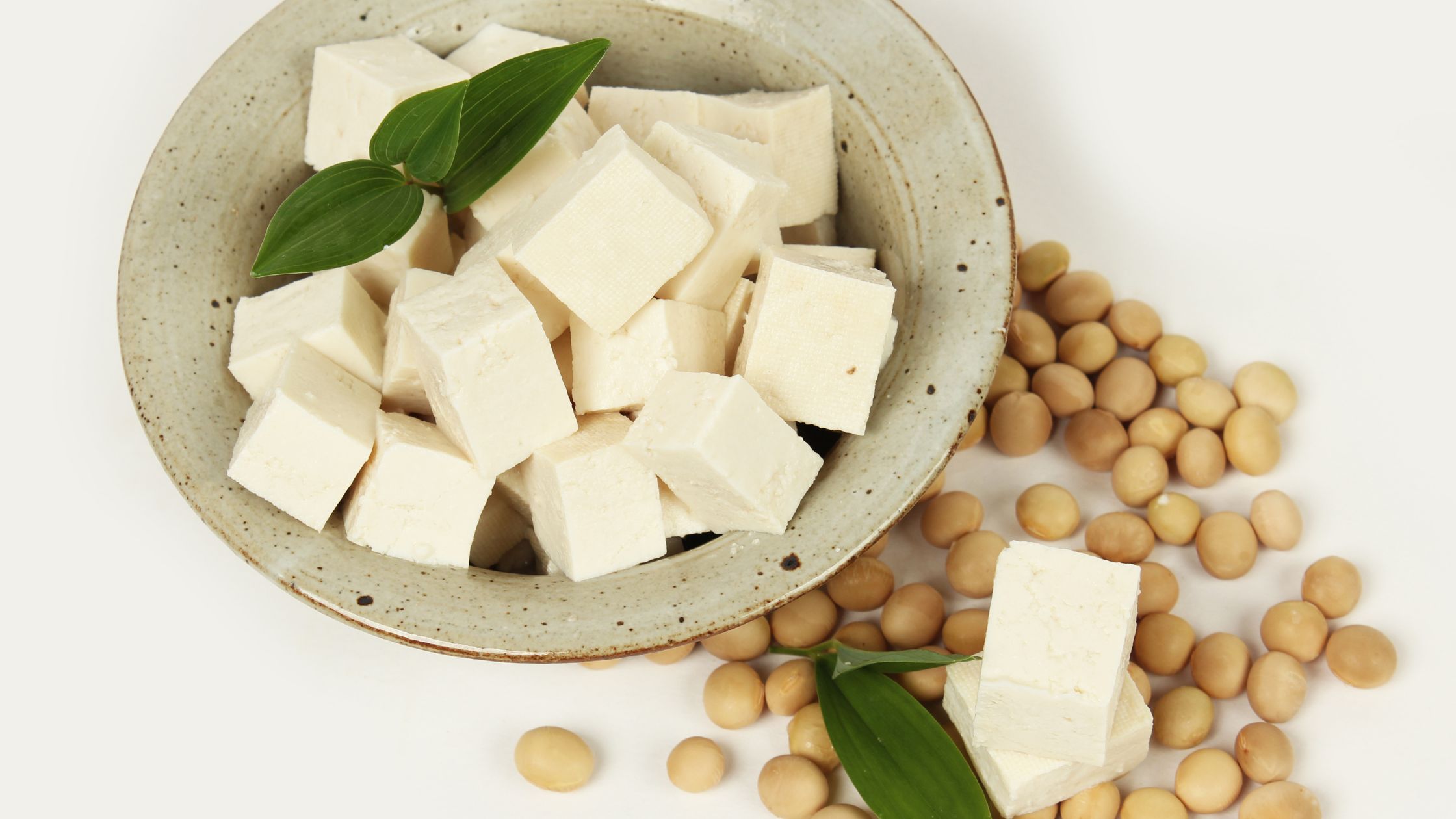 A full bowl of tofu placed on the table along with soy beans.