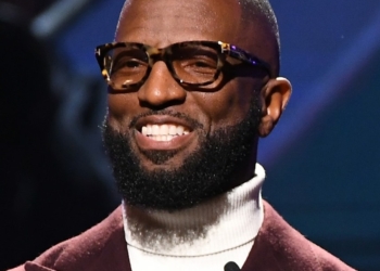 Rickey Smiley wearing white inner and marron colored coat.