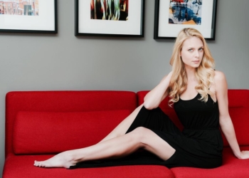Sara Mitich wearing a black dress and posing on a couch.