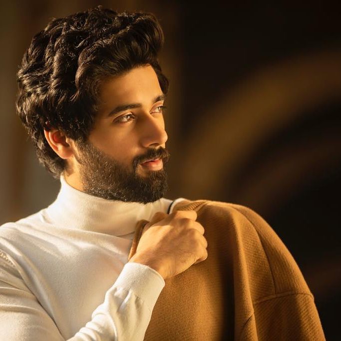 Utkarsh wearing white cardigan and holding brown colored jacket in his hand.